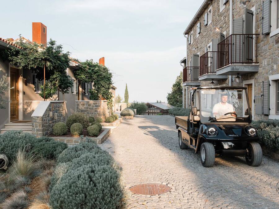 A cobblestone street with a parked vehicle and a building with stone walls and a balcony.
