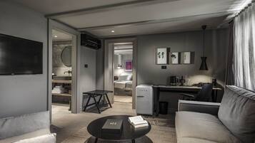Een moderne hotelkamer met een bank, een rond salontafeltje, een bureau met een computer, een minibar en een televisie aan de muur.