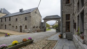 Un edificio de piedra con un patio, un sendero pavimentado y parterres de flores.
