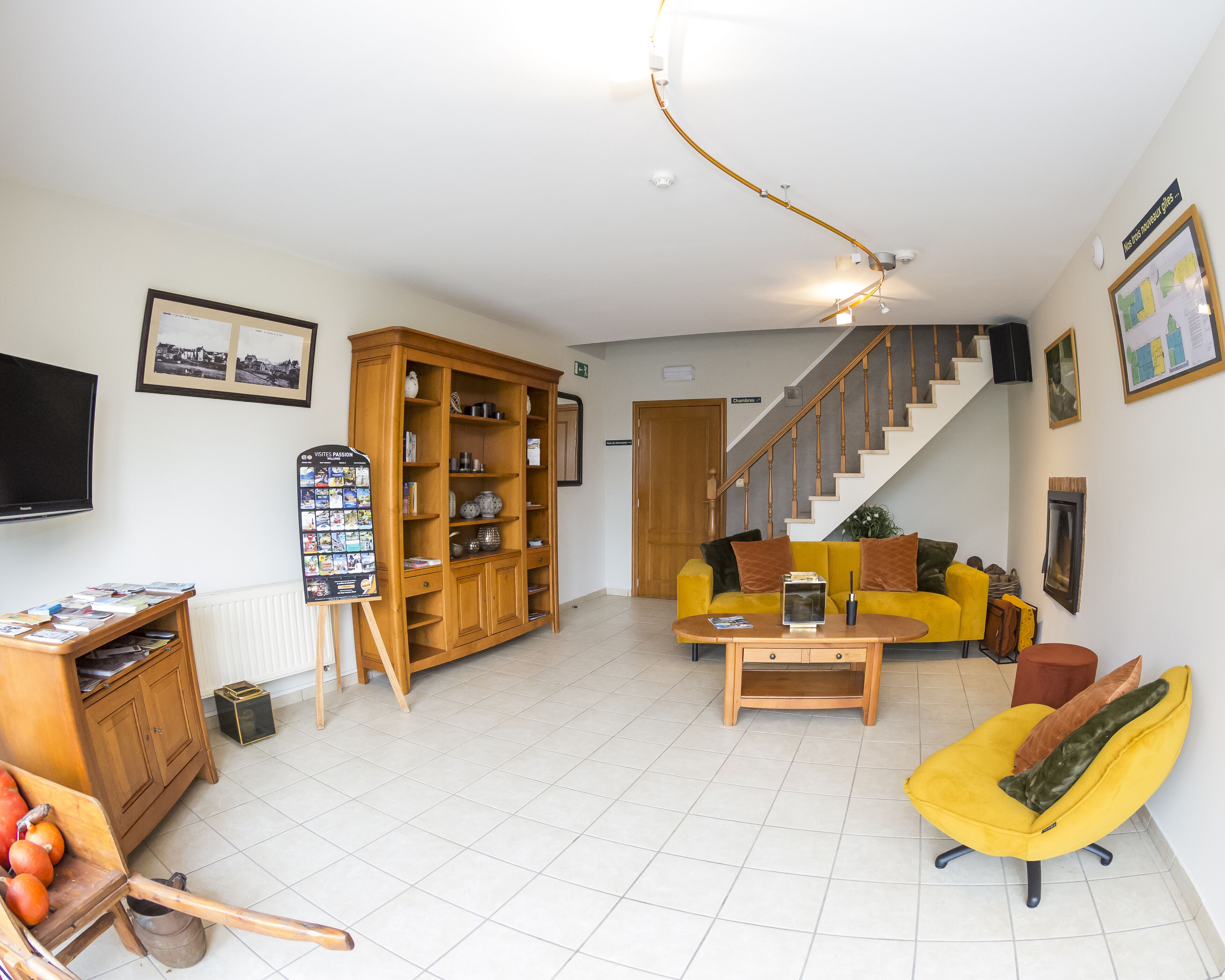 A spacious living room with a yellow sofa, a wooden cabinet, a television, and a staircase leading to another room.