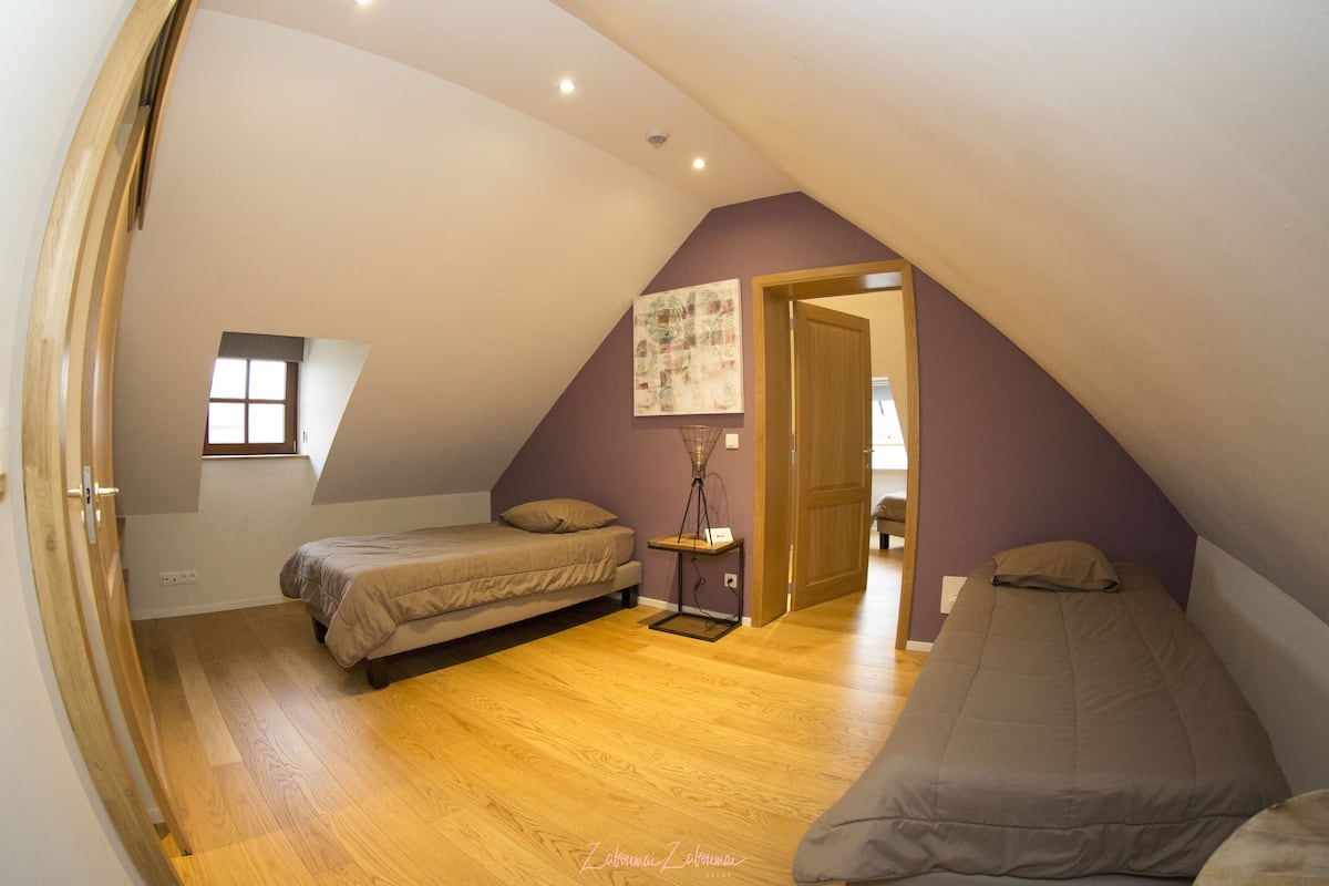 Ein kleines, dreieckiges Schlafzimmer im Dachgeschoss mit zwei Betten, einem Fenster und einer Tür zu einem anderen Raum.