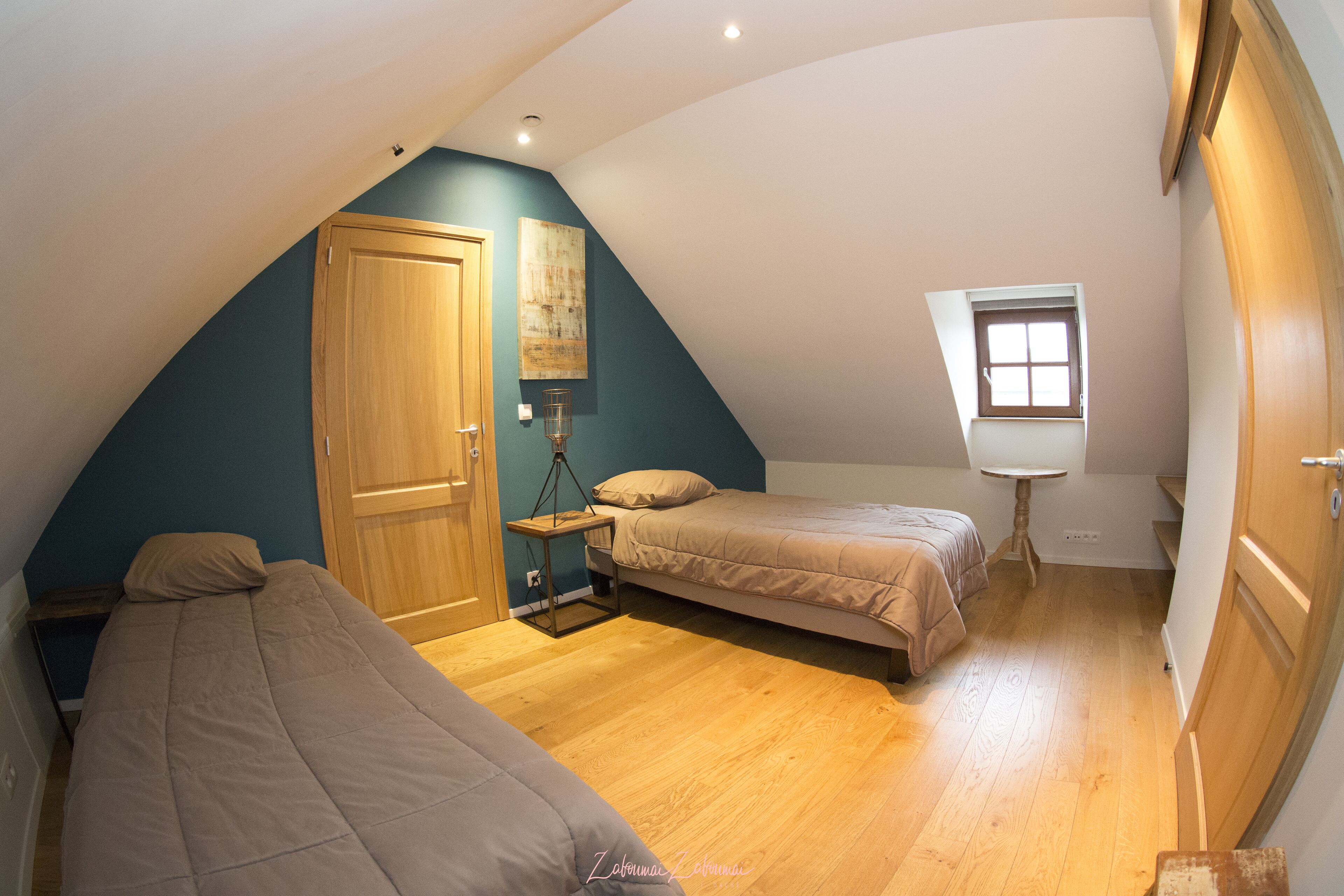 Ein kleines, dreieckiges Schlafzimmer im Dachgeschoss mit zwei Betten, einer Holztür, einem Fenster und einem Bild an der Wand.
