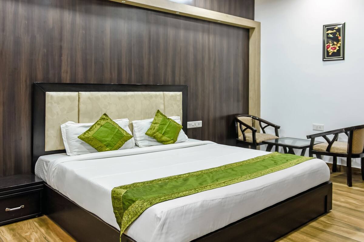 A neatly made bed with white bedding and green accents, a small table with chairs, and a wooden headboard.