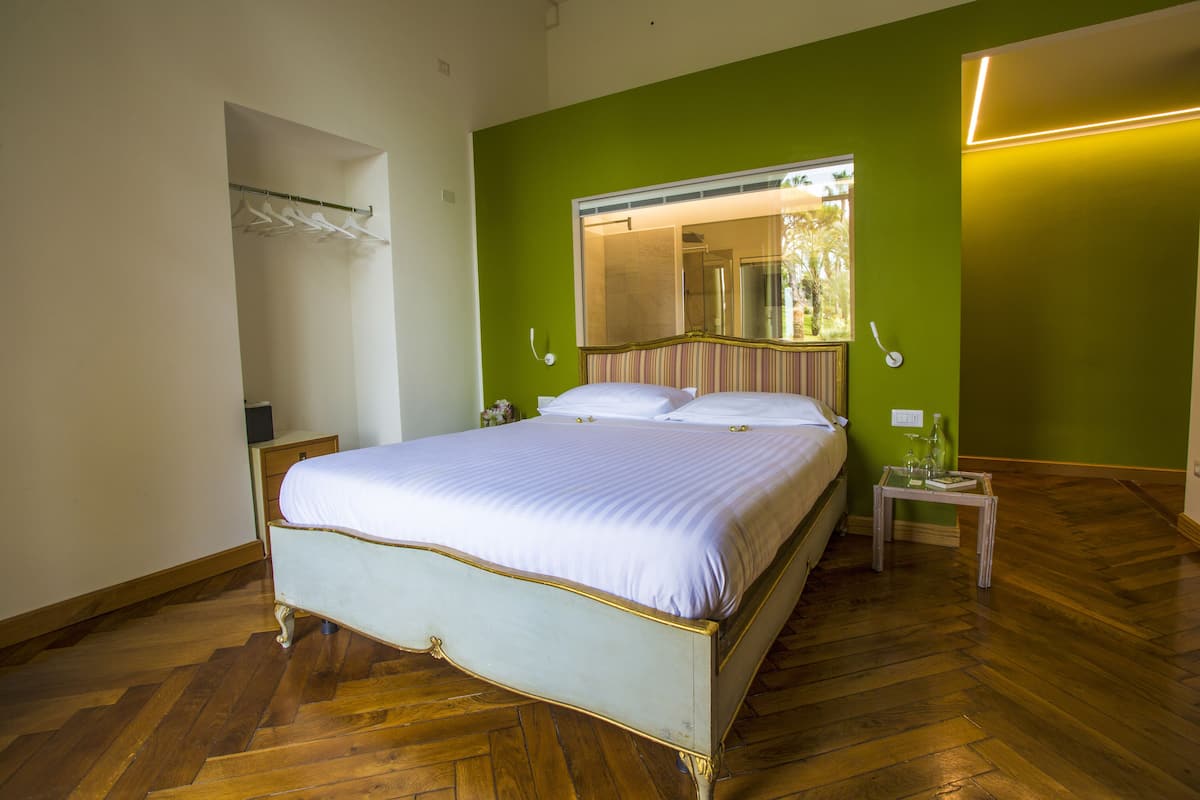 Una cama bien hecha con cabecera, una mesita de noche con lámpara y un espejo sobre la cama.