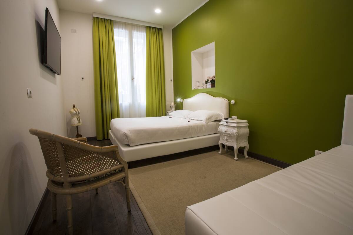 Habitación de hotel con cama, una silla, mesita de noche, espejo y televisión montada en la pared.