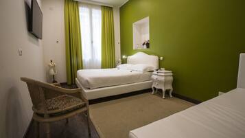 Habitación de hotel con cama, una silla, mesita de noche, espejo y televisión montada en la pared.