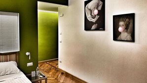Una habitación de hotel con una cama, una mesita de noche con una botella y un control remoto, una pared verde y dos cuadros en la pared.