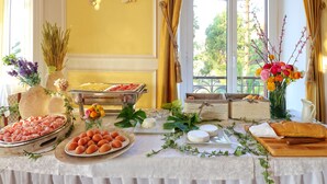 Una mesa de buffet con diversos alimentos, un jarrón con flores y vistas al exterior a través de amplias ventanas.