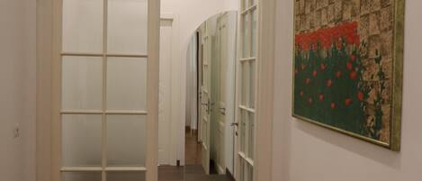 A hallway with a wooden herringbone floor, a frosted glass door, and a framed artwork on the wall.