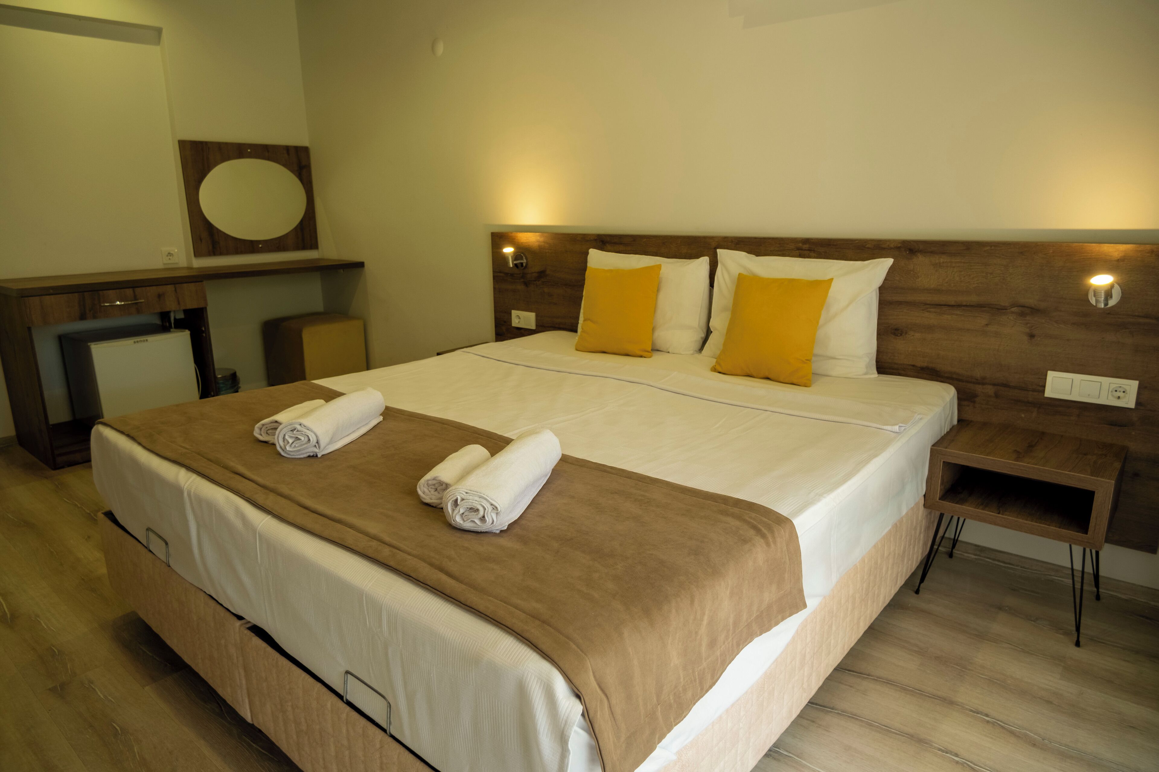 A hotel room with a large bed, two bedside tables, a wooden headboard, and a small desk with a chair.