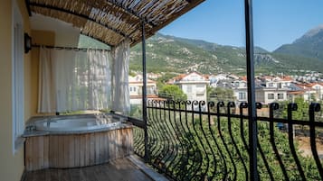 Un balcón con un jacuzzi, vistas de un paisaje montañoso y un techo de paja.