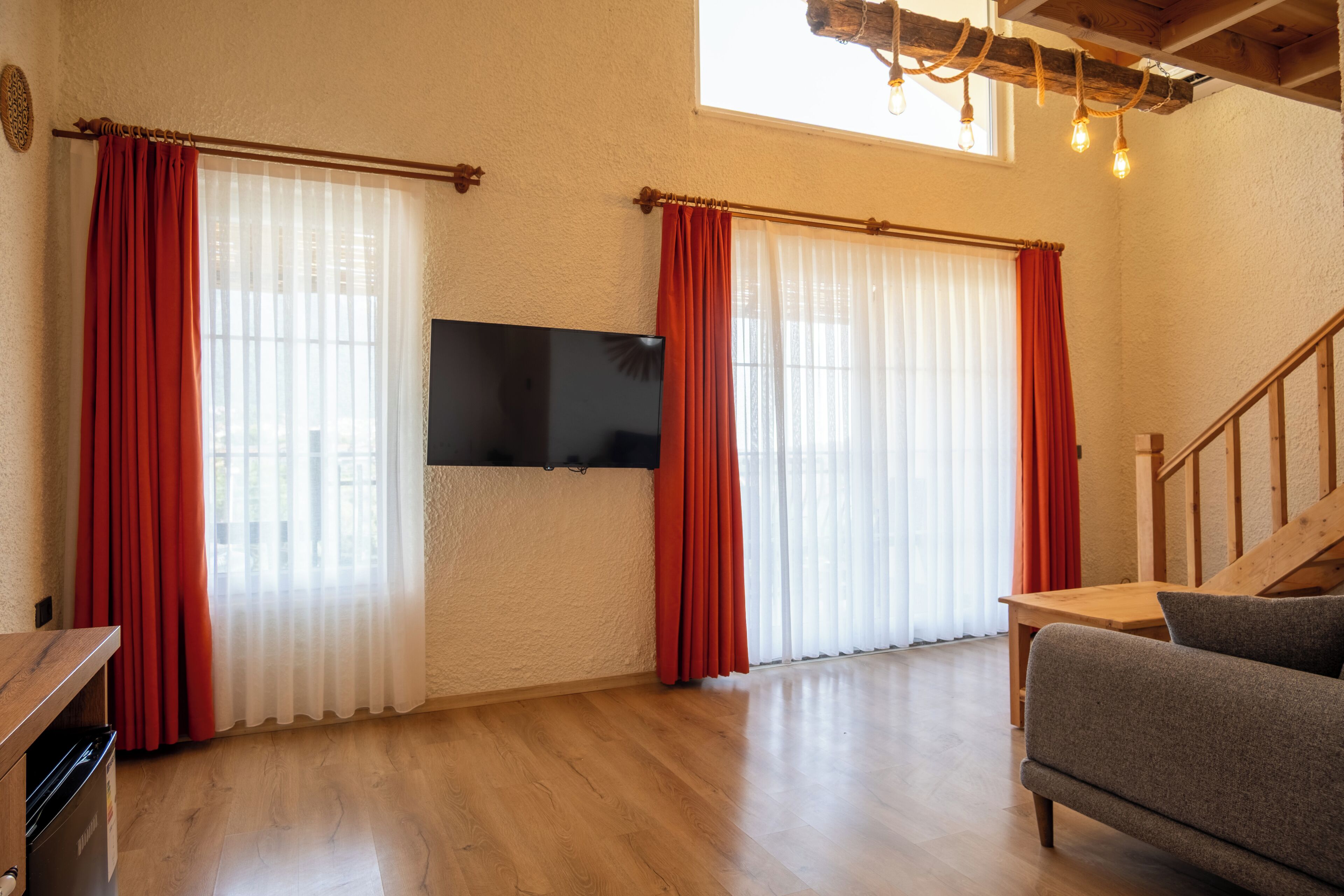 A living room with wooden flooring, a flat-screen TV mounted on the wall, and a staircase leading to an upper level.
