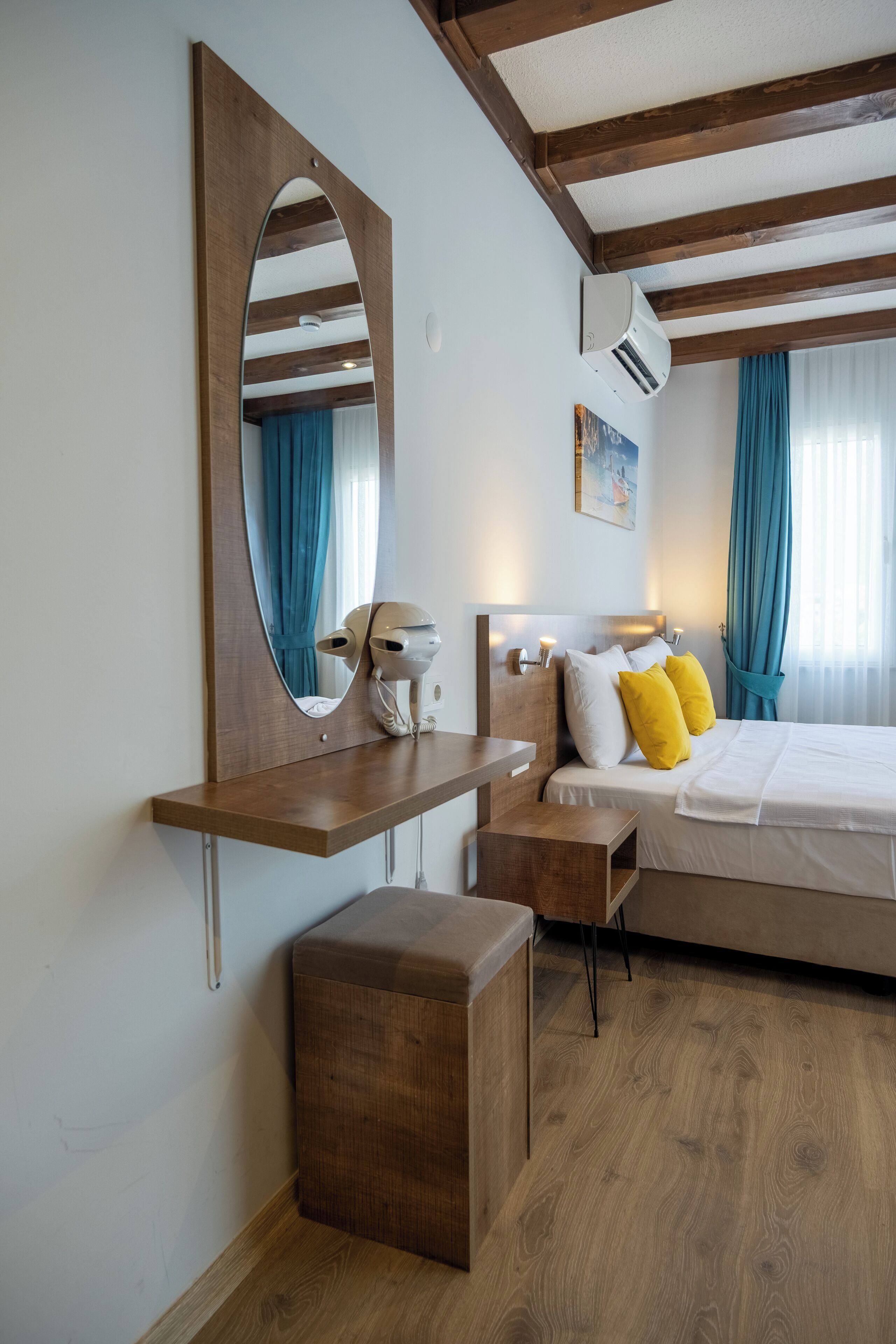 A bedroom with a bed, bedside table, mirror, and a small wooden stool.