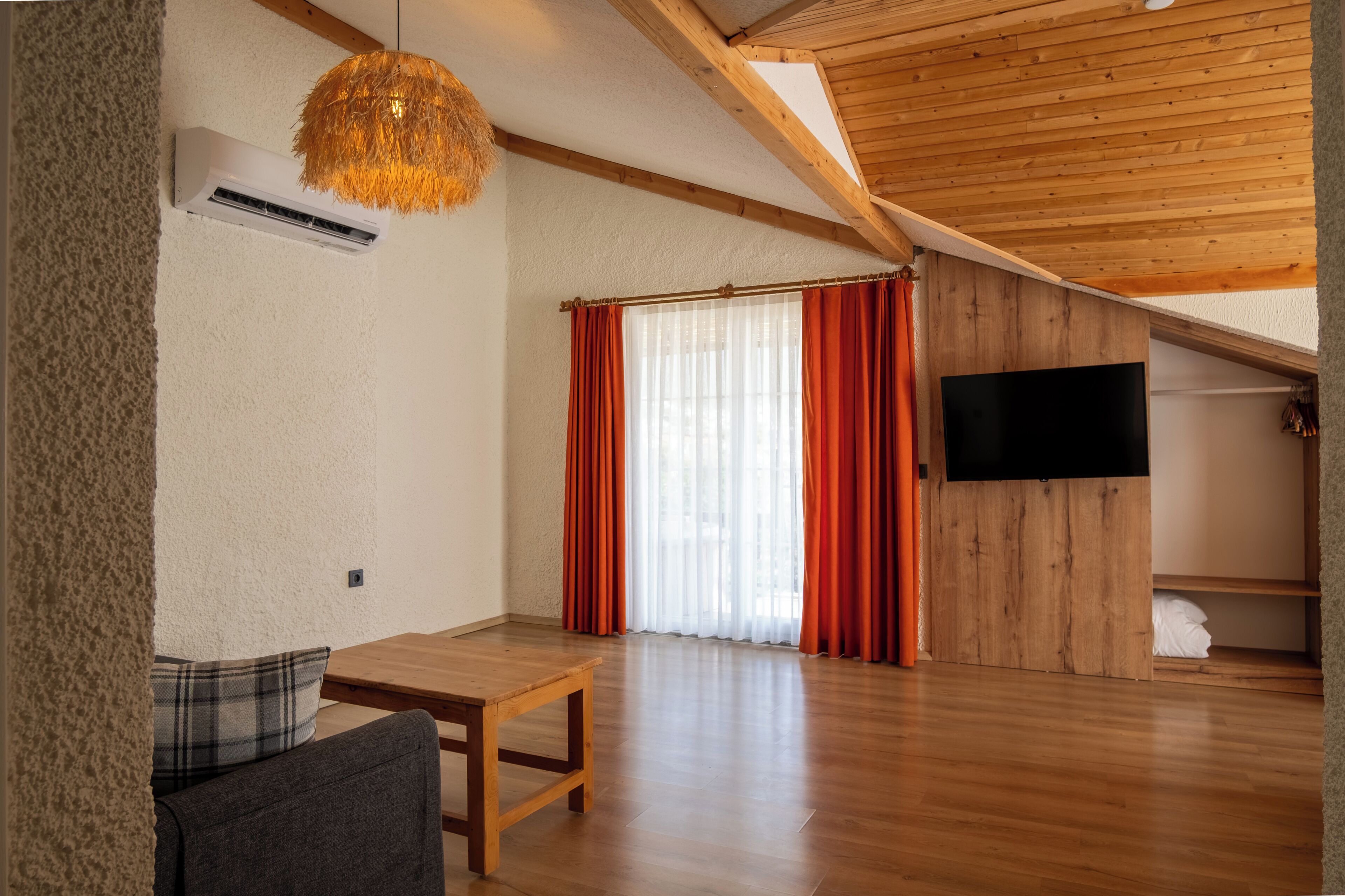 Ein großzügiger Wohnbereich mit Holzboden und einer Holzwand, an der ein Flachbildfernseher angebracht ist, sowie ein großes Fenster mit roten Vorhängen.