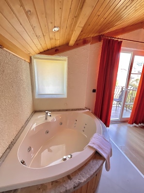 Un baño con una bañera independiente, una ventana y vistas al balcón exterior.
