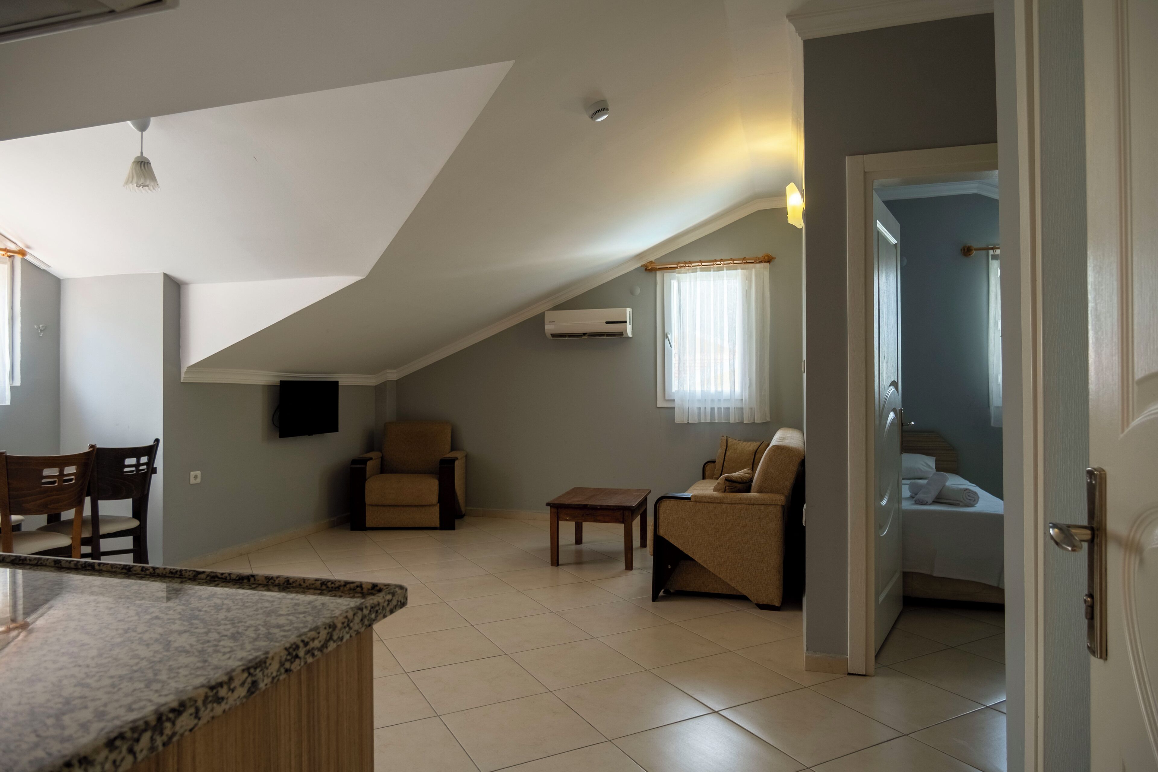 A spacious living area with a high ceiling, a kitchen counter, a sofa, a coffee table, and a door leading to a bedroom.