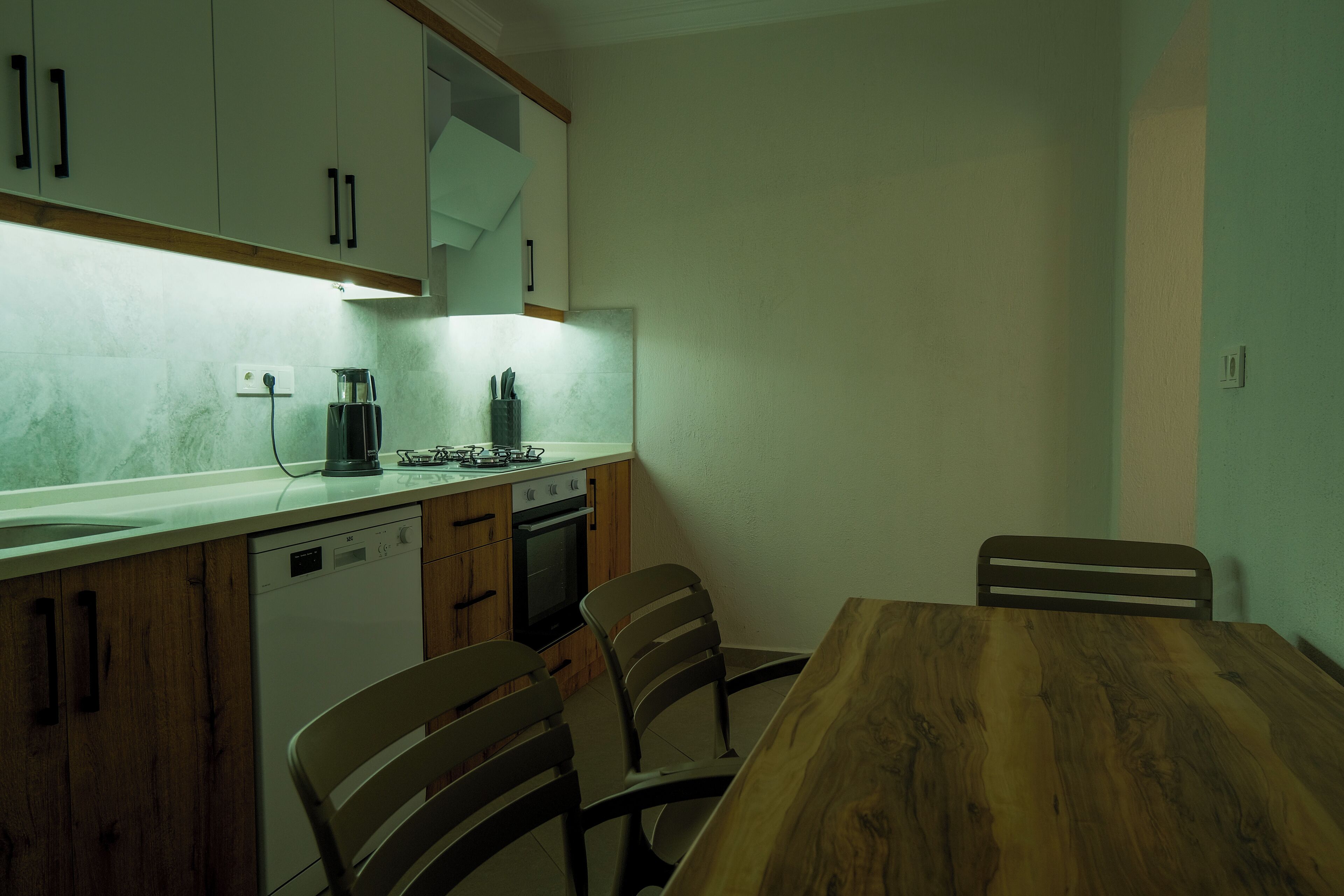 A compact kitchen with wooden cabinets, a dishwasher, an oven, and a dining table with chairs.