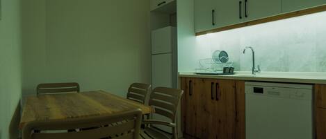Una cocina compacta con una mesa y sillas de madera, armarios blancos, lavavajillas integrado y salpicadero de mármol.
