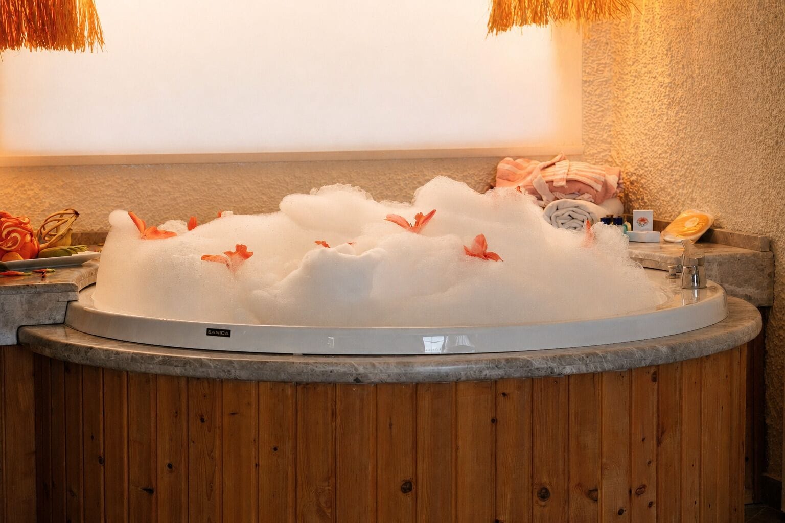 Un jacuzzi con base de madera, rodeado por un muro de piedra y un techo de madera con una lámpara de techo de paja.