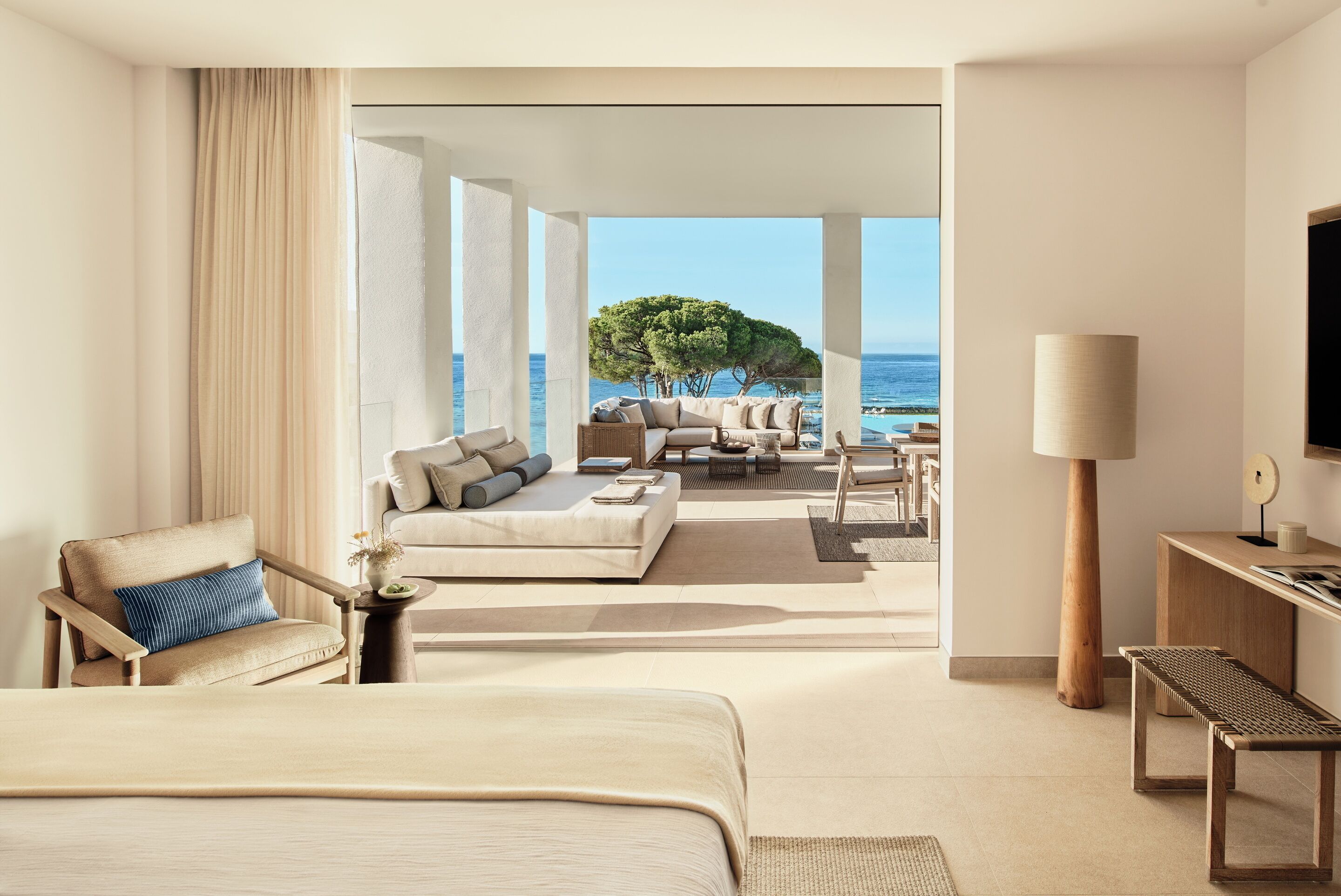 A modern hotel room with a large bed, a sofa, a coffee table, and a view of the sea.