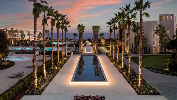 A resort with a pool, palm trees, and a sunset sky.
