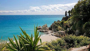 A coastal landscape with a beach, rocky outcrops, and dense greenery.