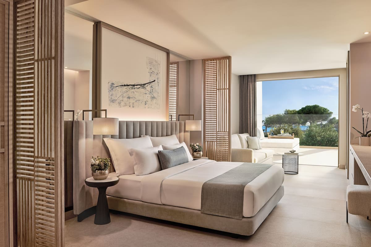 A modern hotel room with a large bed, a view of the outdoors, and a balcony.