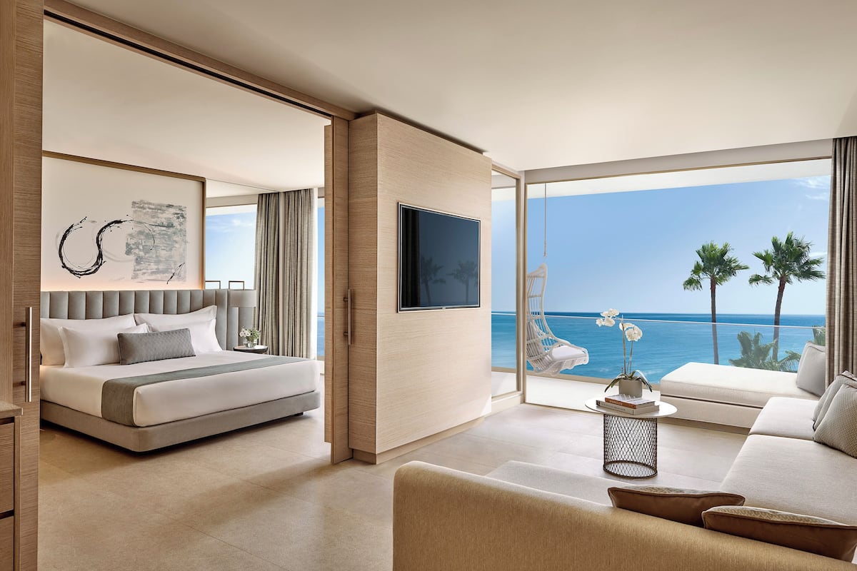 A modern hotel room with a bed, a TV, a sofa, and a view of the ocean.