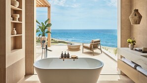 A modern bathroom with a freestanding bathtub, wooden shelves, and a view of the ocean.