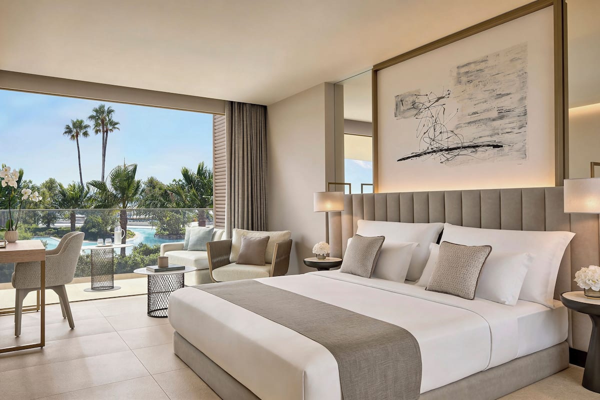 A modern hotel room with a large bed, a dining area, and a view of a pool.