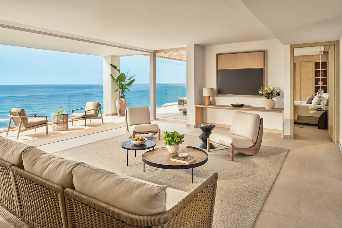 A modern living room with a view of the sea, furnished with sofas, chairs, and a coffee table.