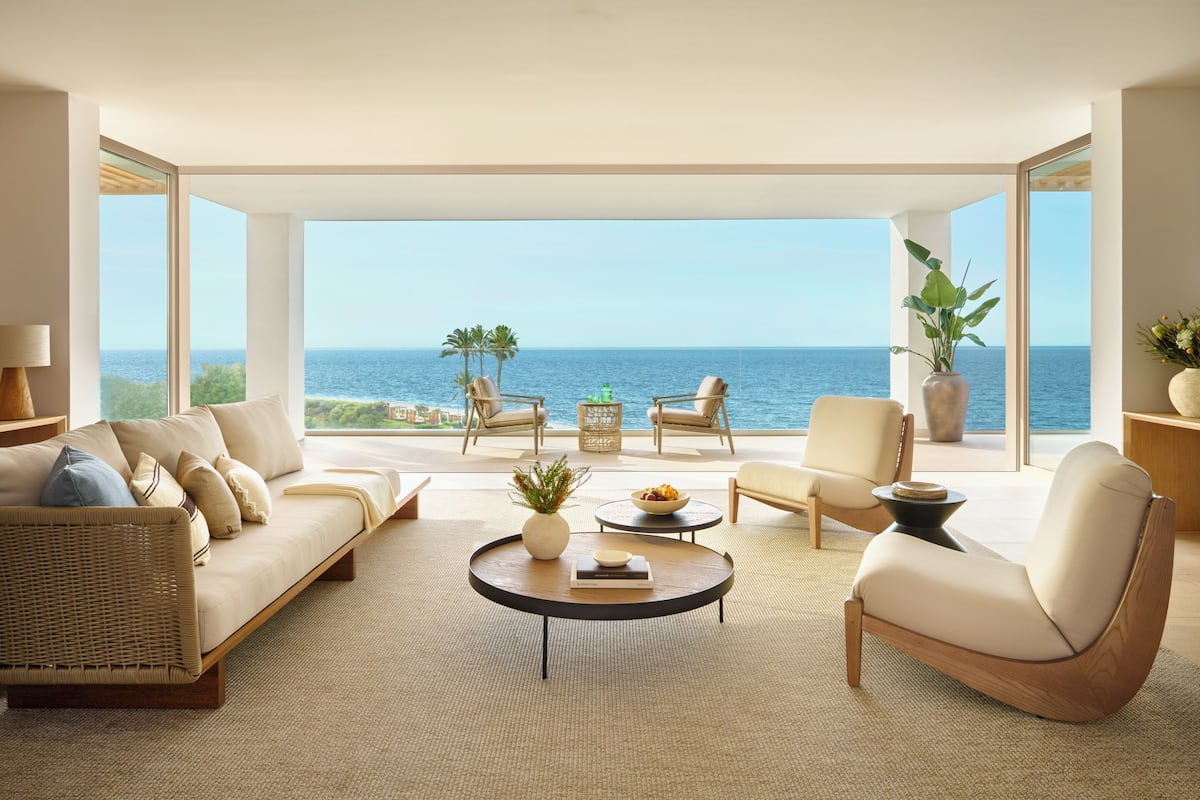 A modern living room with a large window overlooking the sea, a sofa, armchairs, and a coffee table.