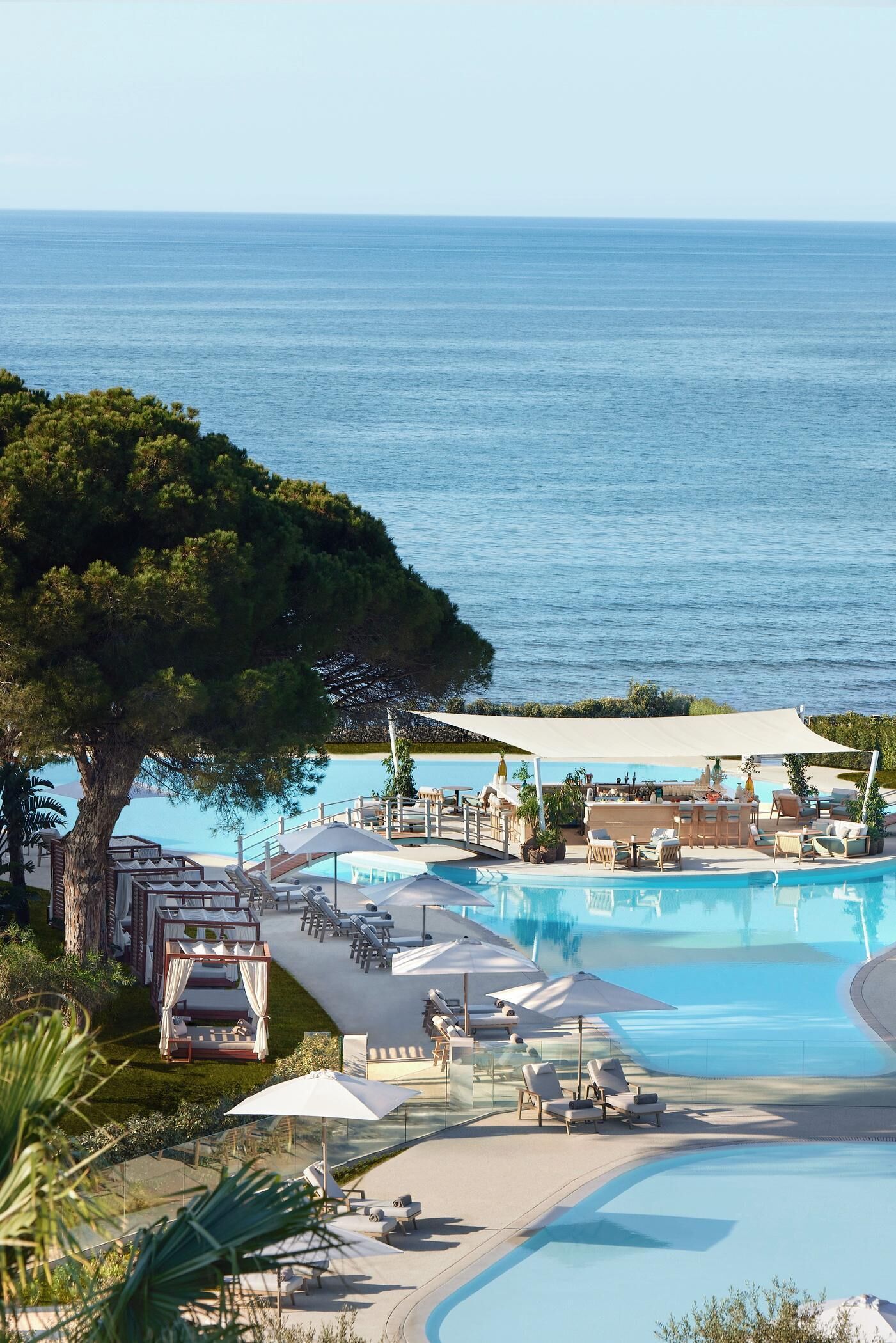 Zona de piscina con sillas de descanso, una cabaña y vista al mar.