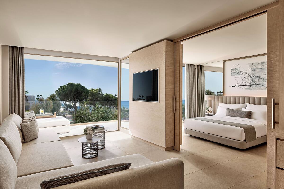 A modern hotel room with a sofa, a bed, a TV, and a balcony with a view.