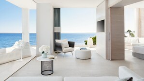 A modern living room with a view of the sea, featuring a sofa, a chair, a round coffee table, and a TV.