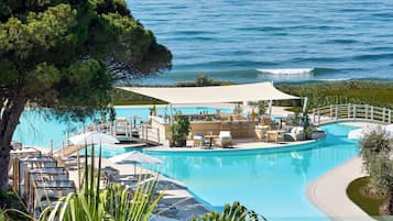 Piscina de un resort con sillones de descanso y un área de bar, rodeada de vegetación y con vista al mar.