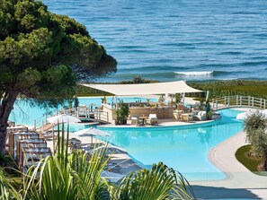 A resort pool with lounge chairs and a bar area, surrounded by greenery and overlooking the sea.