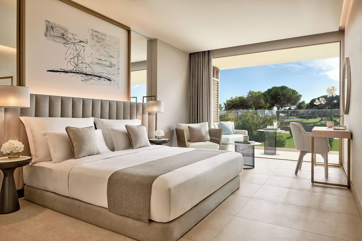 A modern hotel room with a large bed, a desk, and a view of the outdoors.