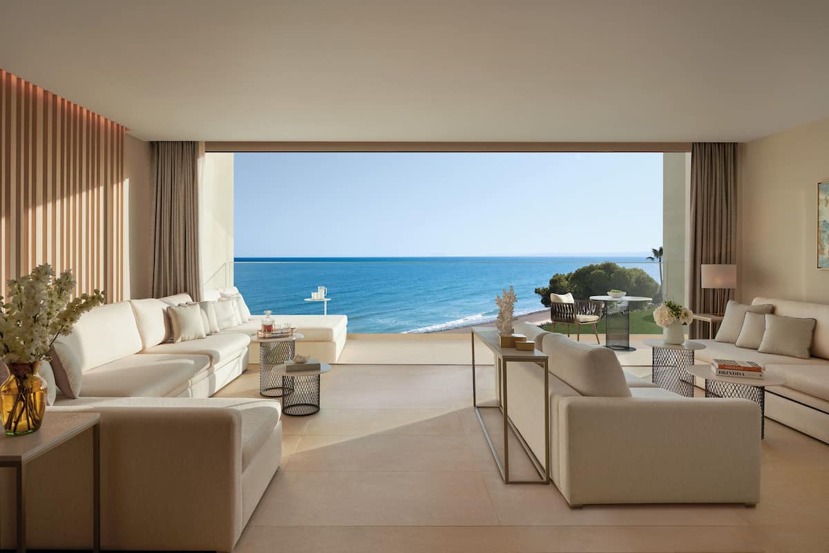 A modern living room with a view of the ocean, featuring a sofa, coffee table, and a dining area.