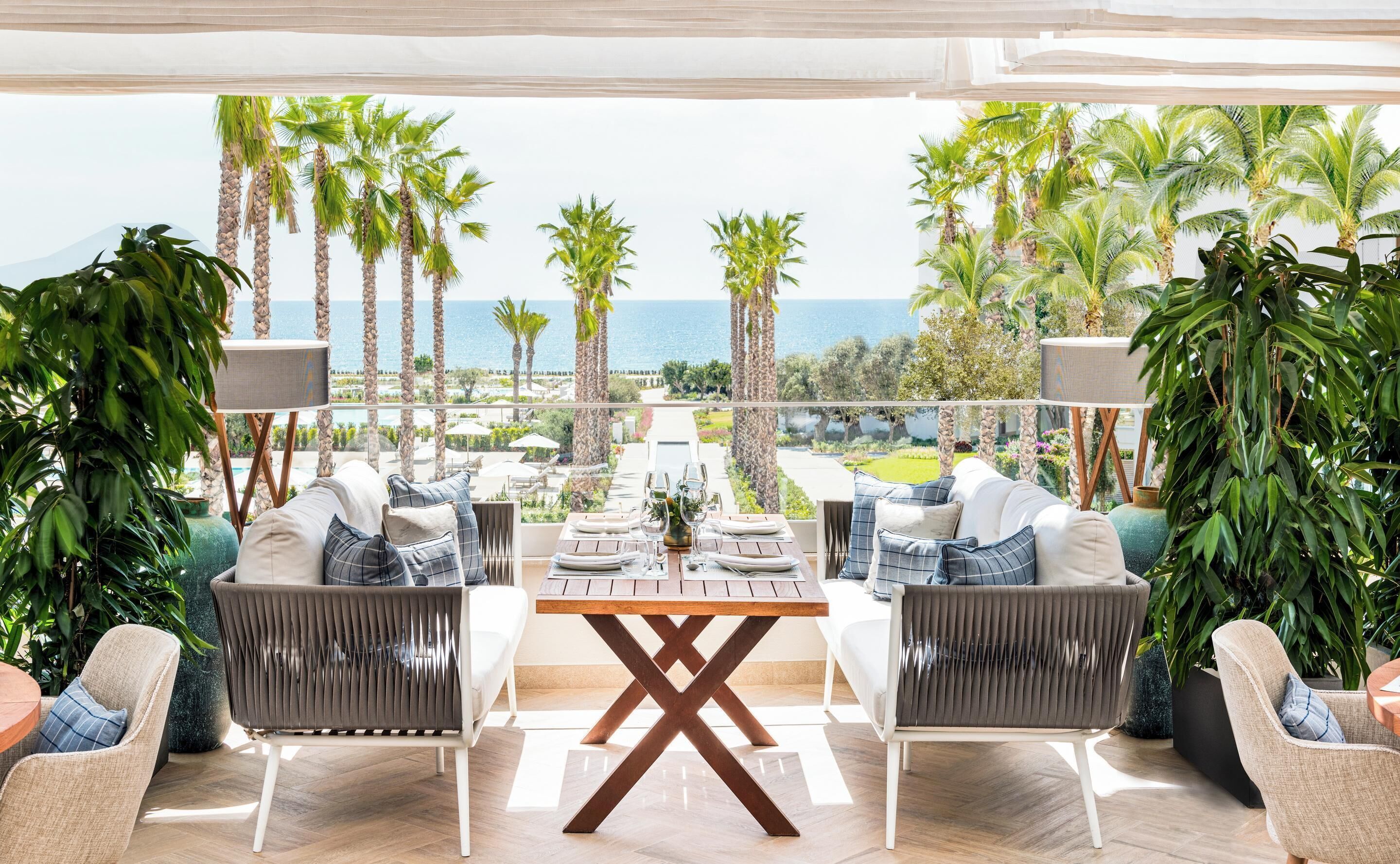 A dining area with a view of the sea, featuring a table set for two, two chairs, and a large window overlooking the ocean.