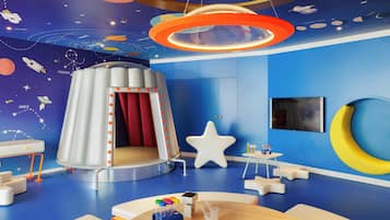 Una habitación con techo decorado con motivos espaciales, una lámpara con forma de estrella, una mesa redonda con un globo terráqueo y un pequeño escritorio blanco.
