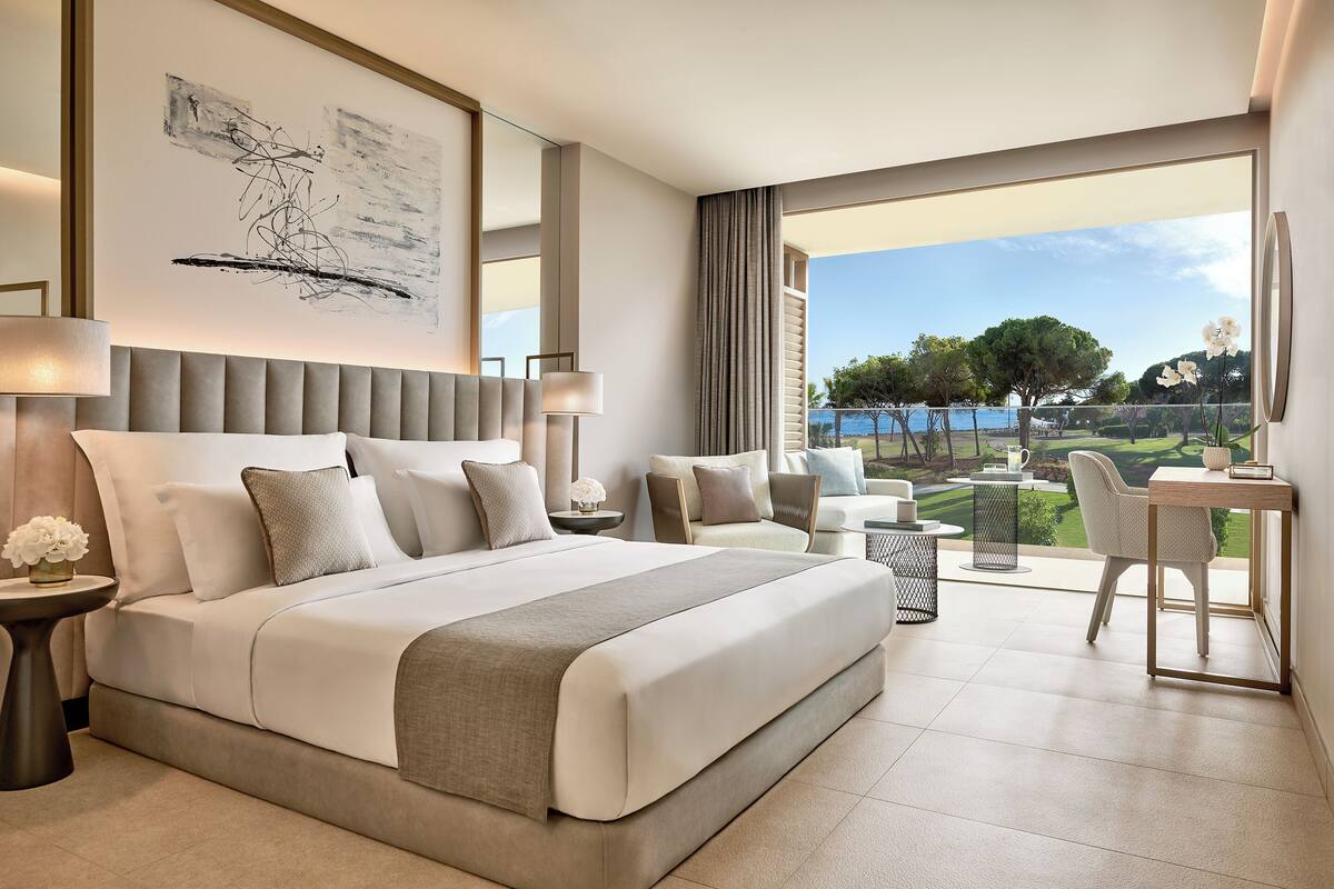 A modern hotel room with a large bed, a desk, and a view of a golf course.