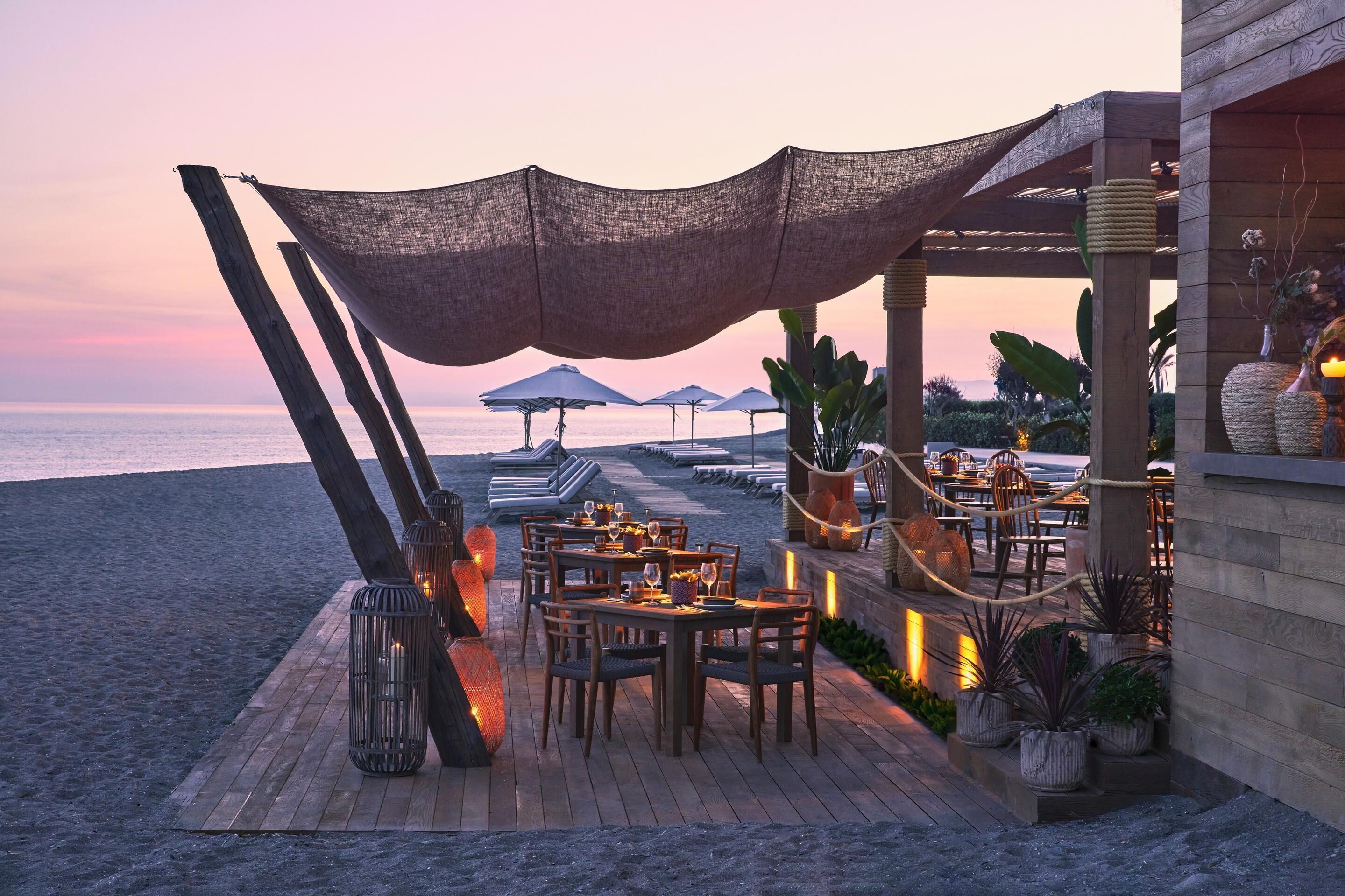Un restaurante frente a la playa con mesas y sillas de madera y vistas al océano.