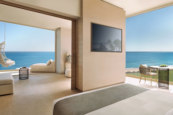 A modern hotel room with a large bed, a television, a seating area with a view of the sea, and a balcony with a table and chairs. - Ikos Andalusia - All Inclusive (Estepona)