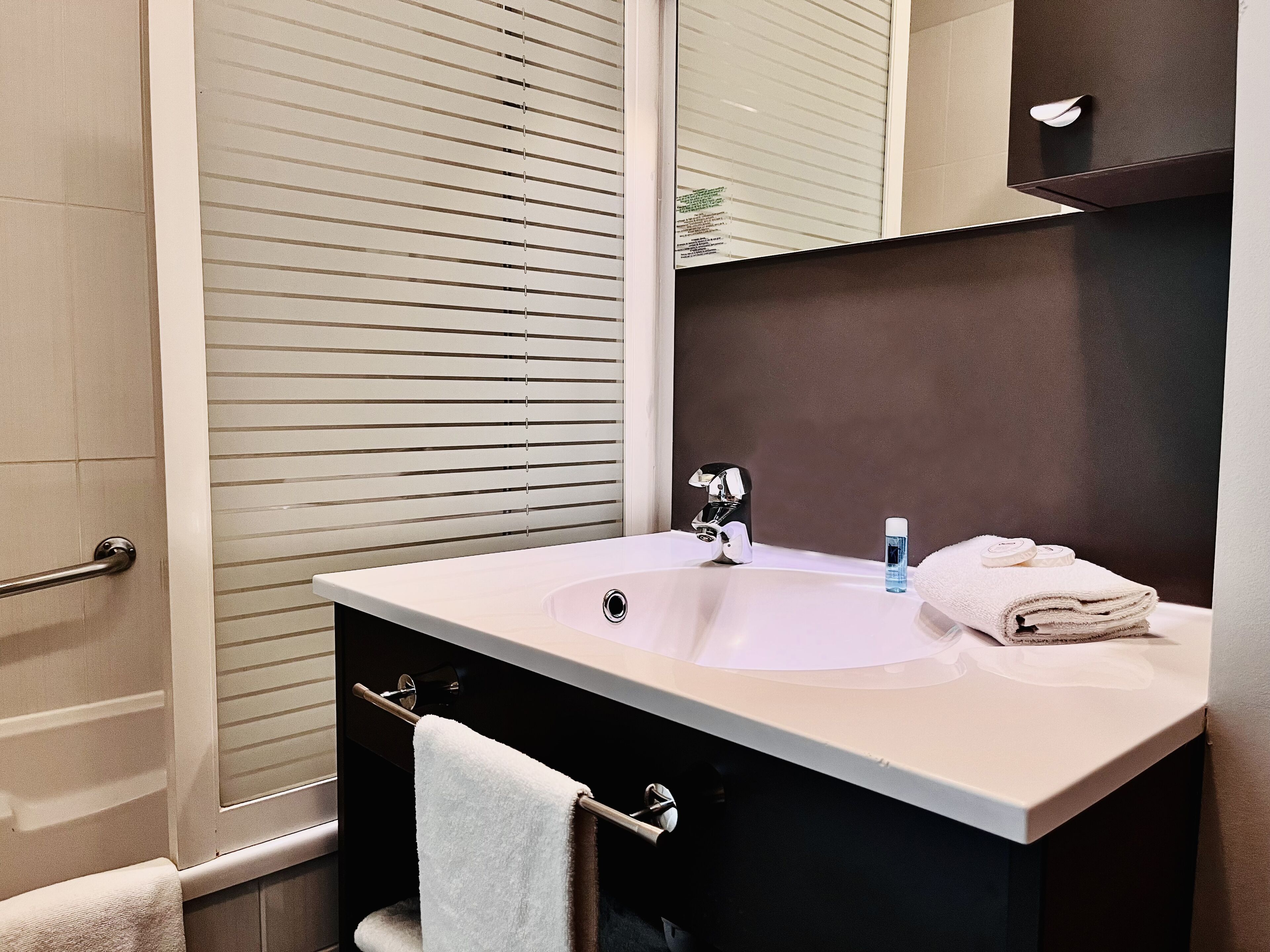 A bathroom with a sink, mirror, towel rack, and a window with blinds.