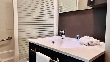 Un baño con lavamanos, espejo, toallero y ventana con persianas.