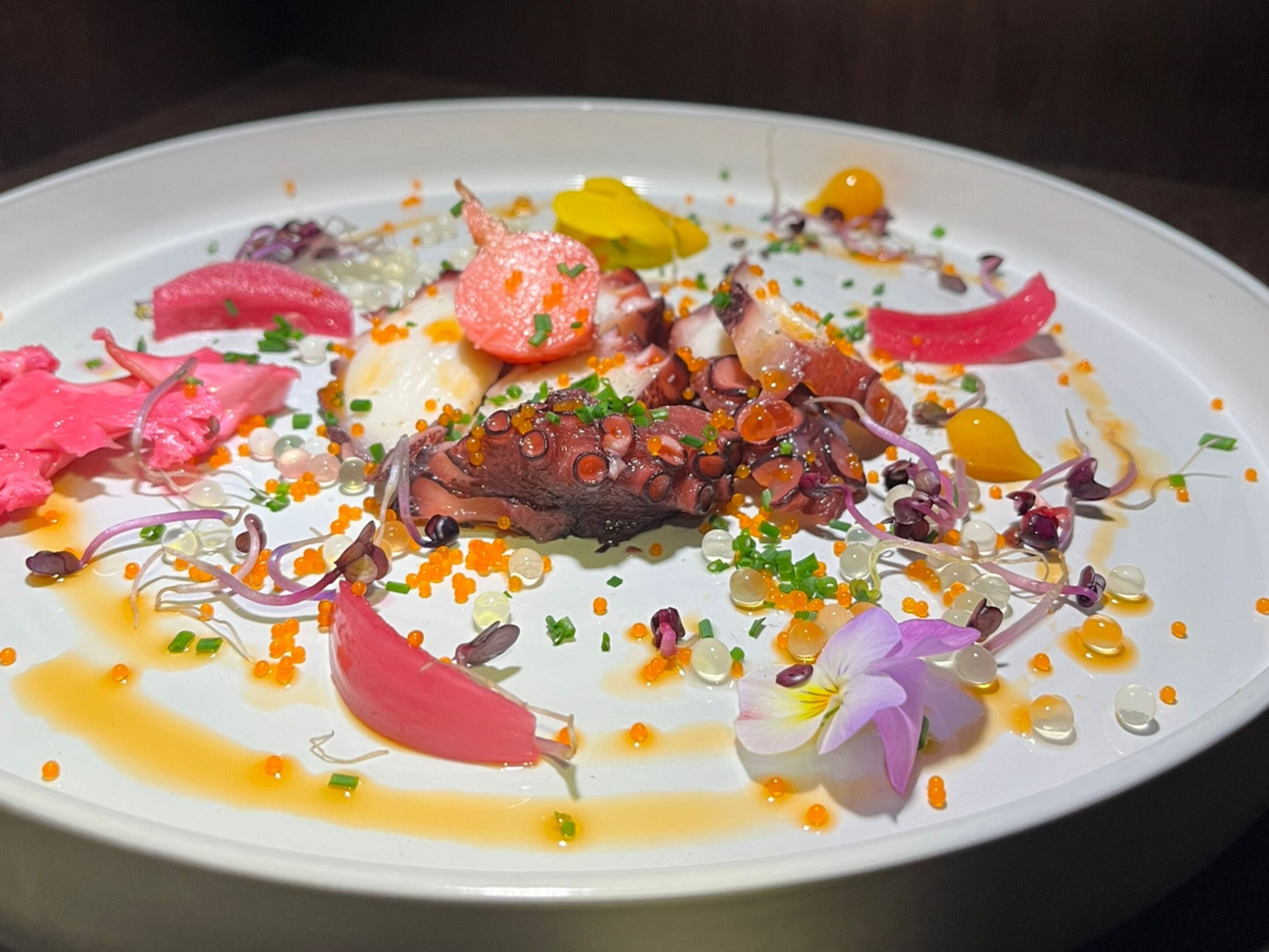 Een wit bord met diverse soorten eten, waaronder octopus, groenten en caviartopping.