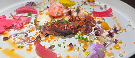 A white plate with a variety of food items including octopus, vegetables, and caviar.