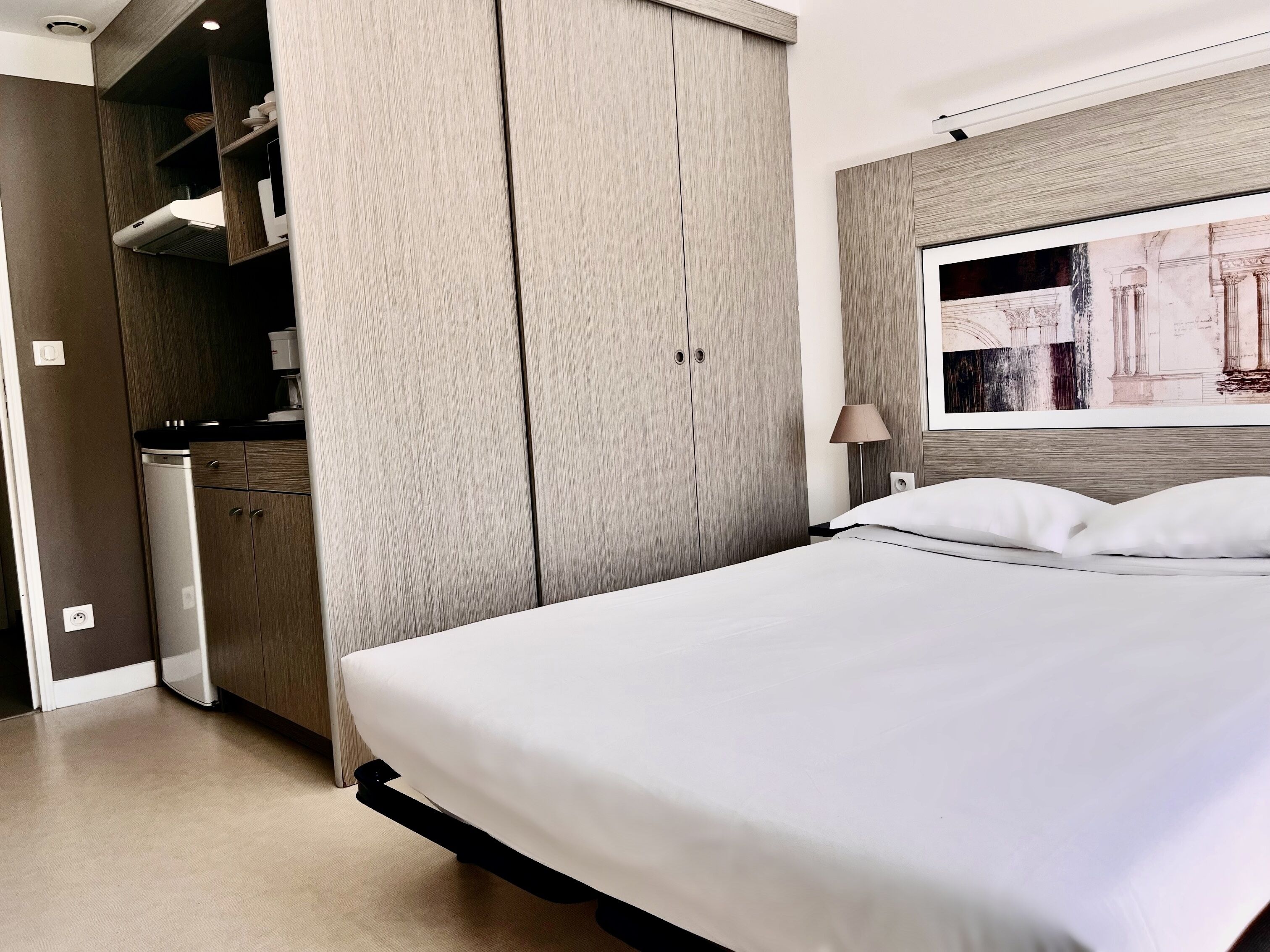 Una habitación de hotel moderna con una cama grande, un armario empotrado y un cuadro en la pared.