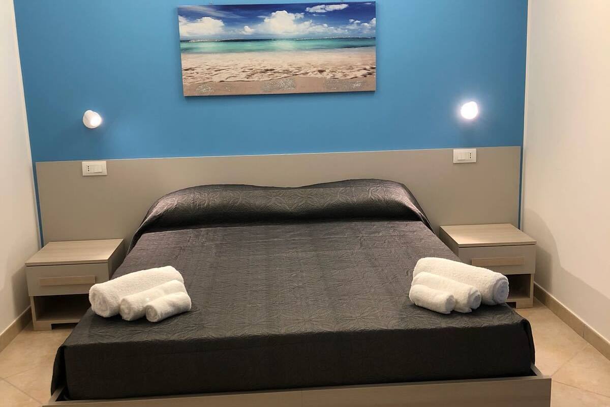 A bedroom with a bed, two nightstands, a painting of a beach, and a skylight.